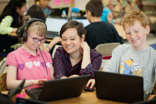 A student teacher works with kids on their laptops