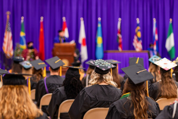 Graduates are seated in rows before the Commencement Ceremony stage.