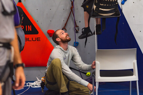 A man helps a person in a wheelchair use adaptive climbing equipment at the WSU Climbing Center.