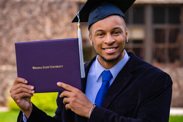 A graduate wearing his cap and gown holds up a diploma after WSU Commencement ceremony.