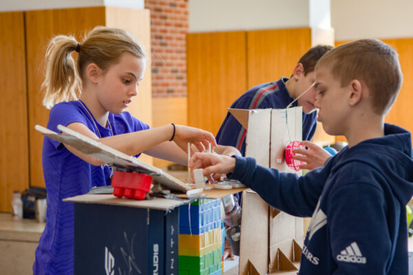 Kids construct an invention with legos, cardboard, and other materials.