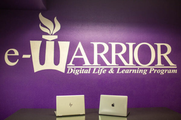 An HP laptop and a Mac laptop sit on a table below a sign that reads 