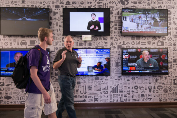 A student talks to a professor while walking down a hallway in Phelps Hall.