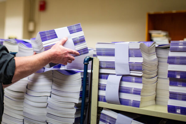 A person grabs a bundle of booklets from a large stack.