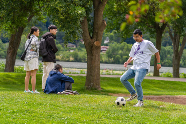 A group of students kick a soccer ball around by Lake Winona.