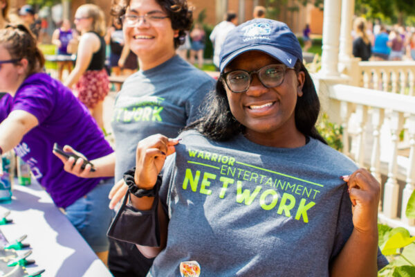 A student club member poses smiling during a campus club fair.