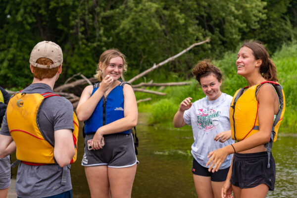 A group of students wearing life jackets stand on a sandbar in the Mississippi backwaters.